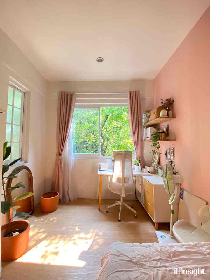 Bright bedroom and home office in white and pink tones featuring desk, office chair, natural light, and plants creating a cozy atmosphere