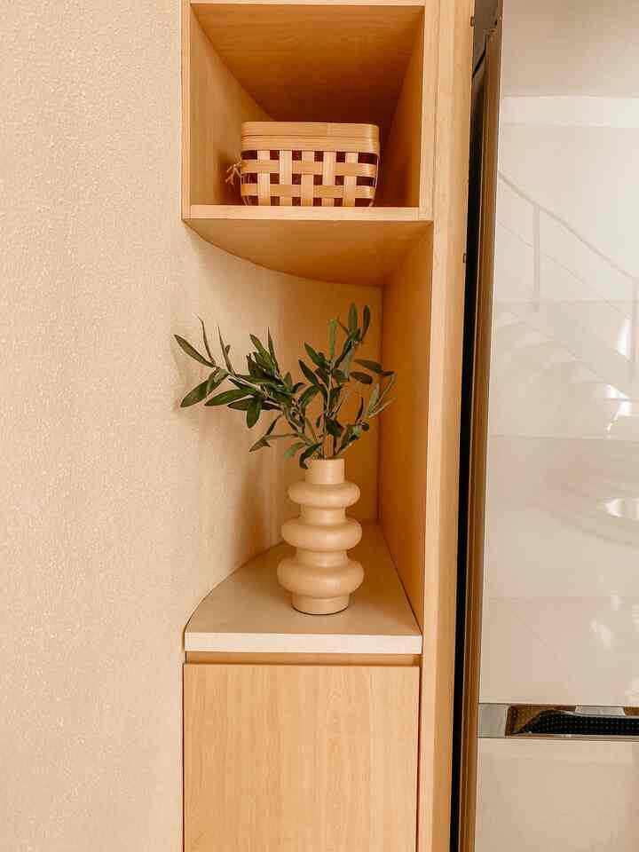 Natural color and wood tone corner storage area featuring beige vase with plant, creating a cozy atmosphere