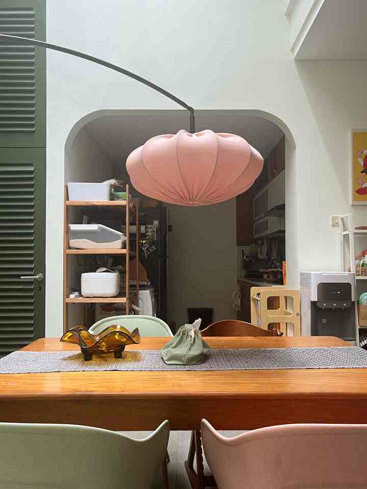 Wood tone and pink-hued dining room featuring a wooden dining table, assorted chairs, and a pink pendant light in a cozy setting