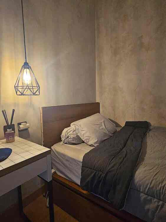 Beige-toned walls and wood-toned bed in a compact bedroom featuring a simple white desk and an industrial pendant light, creating a neat atmosphere