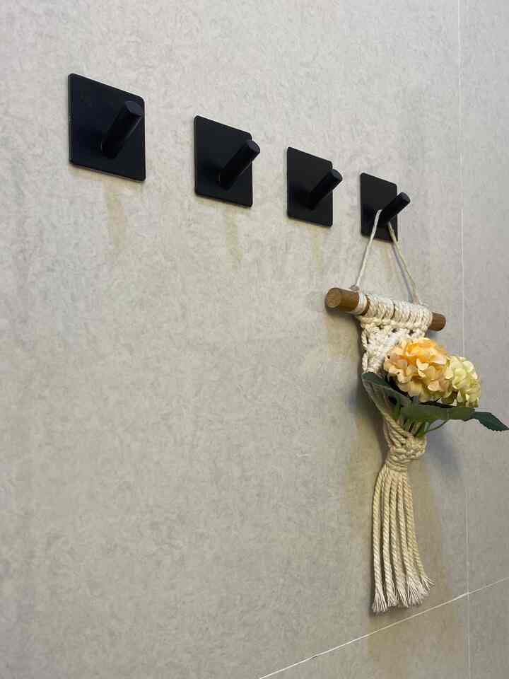 Light gray wall bathroom featuring four black wall hooks and white macramé wall decor with flowers