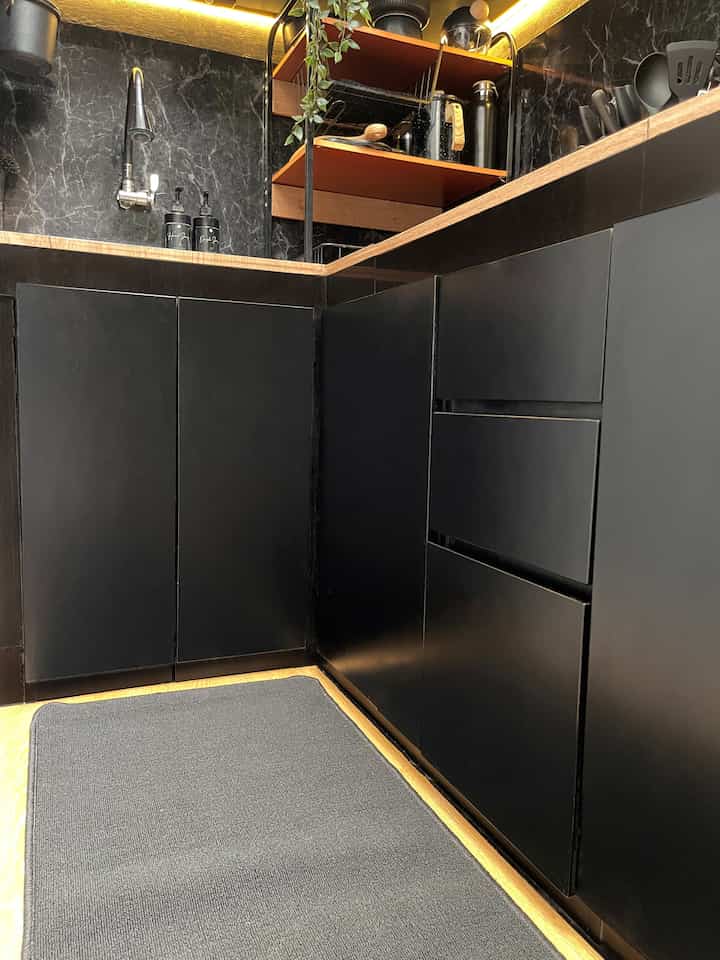 Modern compact kitchen space dominated by black and wood tones, featuring custom cabinetry and a gray kitchen rug creating a cohesive aesthetic