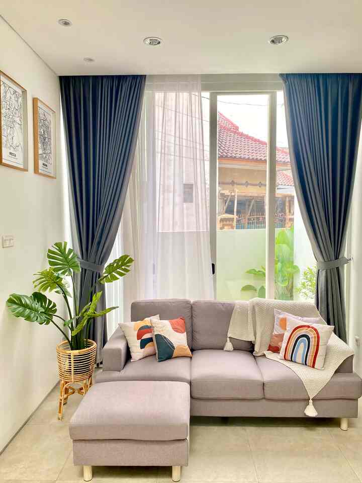 Bright and open living room with white walls, light gray sectional sofa, dark blue blackout curtains on sides, and sheer white curtains in center