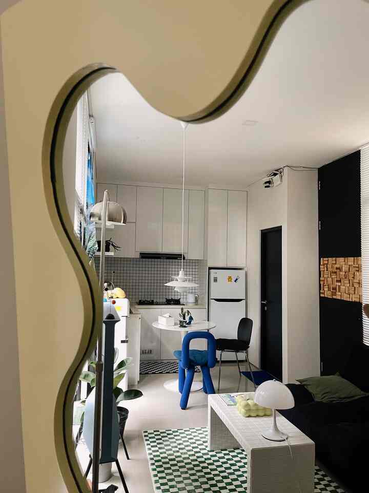 Mid-Century Modern living room and kitchen in white and black tones, featuring a prominent blue chair and a large curvy mirror creating a spacious feel