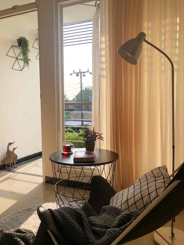 Beige curtains and black furniture arranged in a balcony window relaxation space bathed in warm sunlight, creating a cozy atmosphere