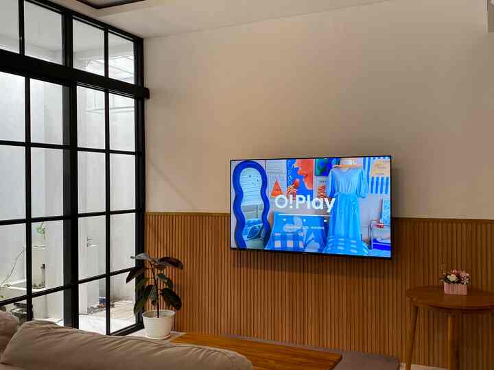 White and wood-tone living room featuring wall-mounted TV, plants, and floor lamp on left side, creating a cozy atmosphere