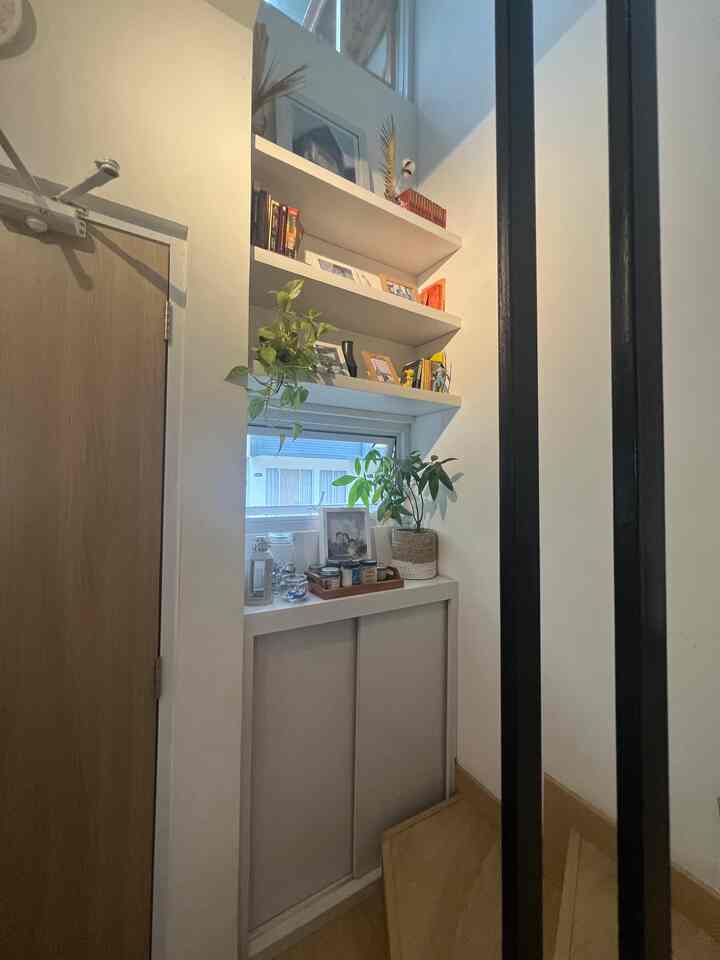 White and wood tone small entrance area featuring corner cabinet and wall shelves with plants, picture frames, and candles creating a cozy atmosphere