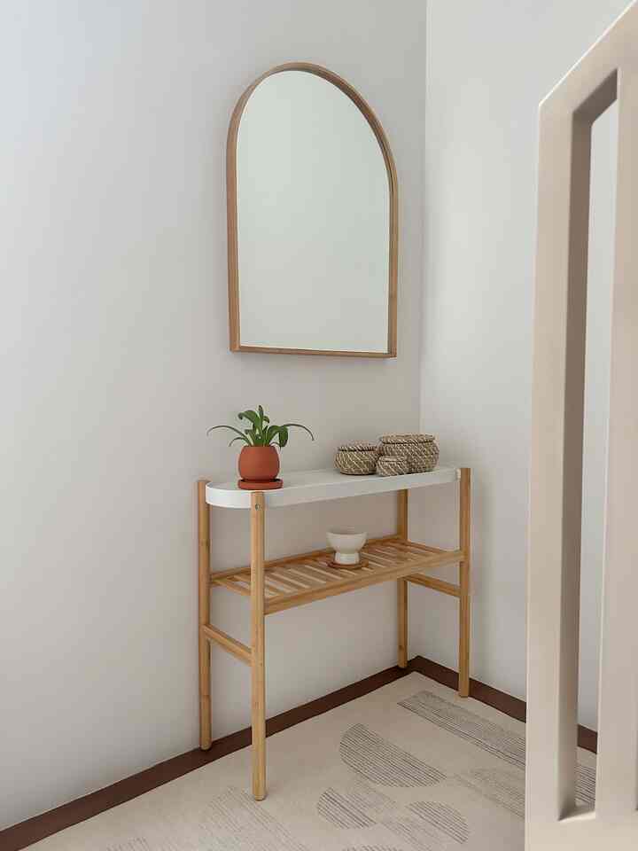 White and beige toned hallway with wooden frame mirror and a shelf adorned with plant and woven baskets, creating a simple natural space