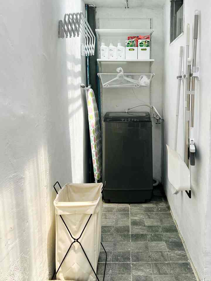White-toned narrow and long indoor laundry space featuring a washing machine and neatly organized storage shelves