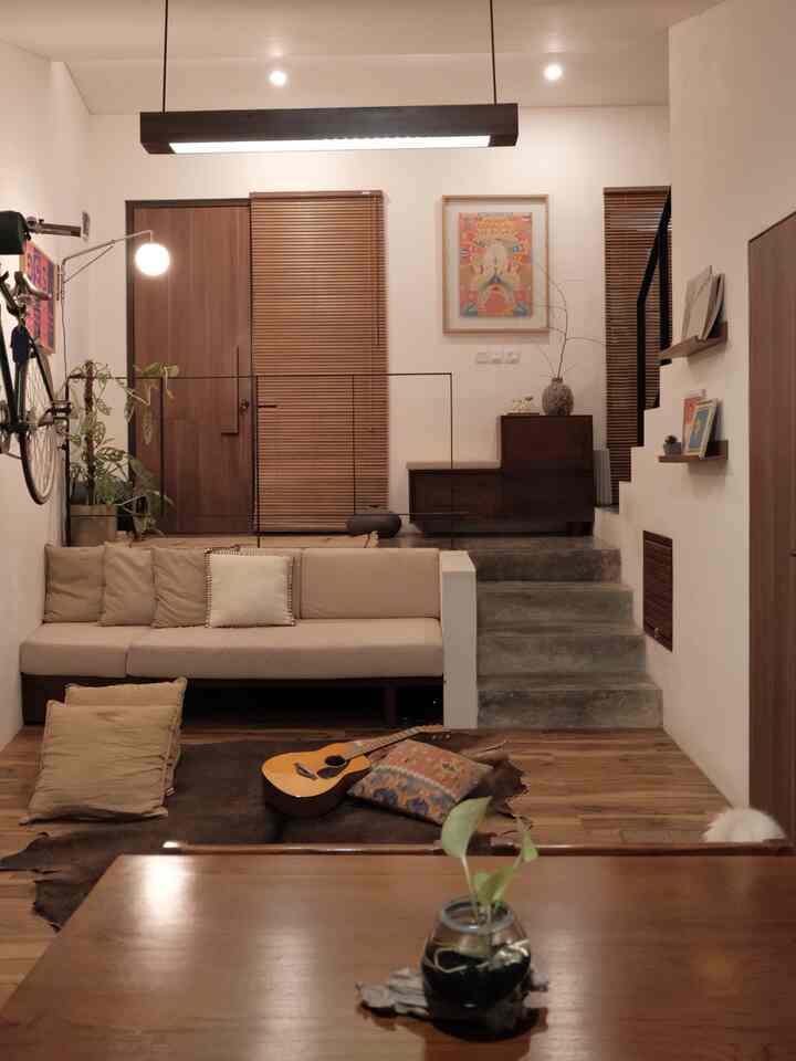 A natural tone small living room featuring beige sofa, wood tone flooring, and wall lighting with a warm cozy atmosphere