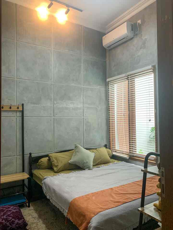 Cozy bedroom with gray concrete wall and green bedding, wooden blinds on window and warm indoor lighting create inviting atmosphere