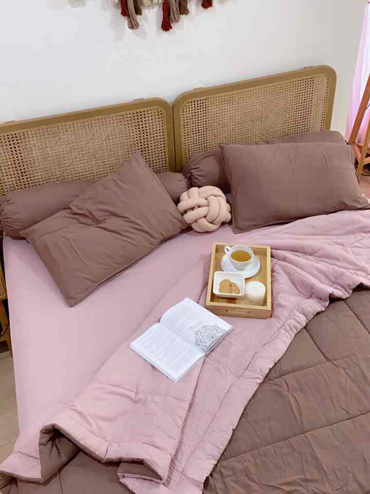 Soft pink and brown toned bedroom featuring woven headboard and a tray with tea, cookies, and a candle for a cozy atmosphere