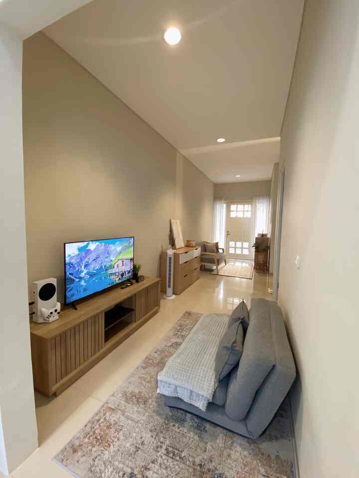 Beige and gray toned narrow living room featuring sofa bed, carpet, and TV stand in a simple natural setting