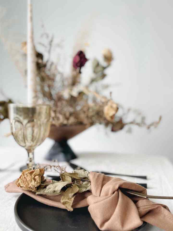 Beige and black dining table setting featuring dried flowers and linen napkin, creating a cozy natural atmosphere