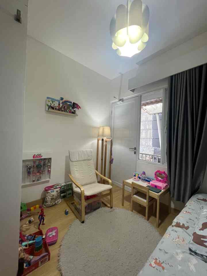 A small kids' room in white and wood tones featuring children's toys, a kid’s desk, and a comfortable armchair in a simple setting