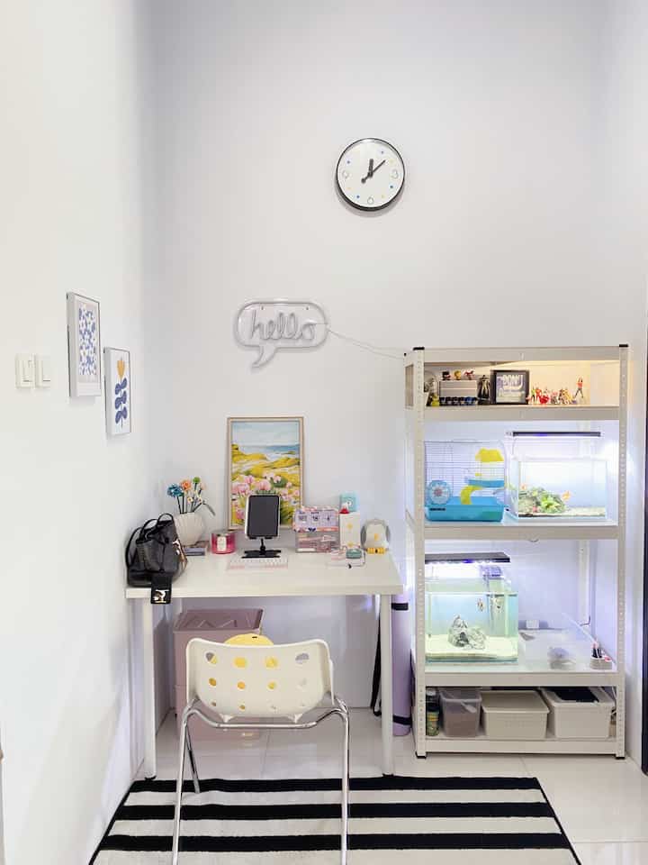 White and black toned home office space featuring a desk and chair center-left and pet cages with shelving on right, minimalist compact interior