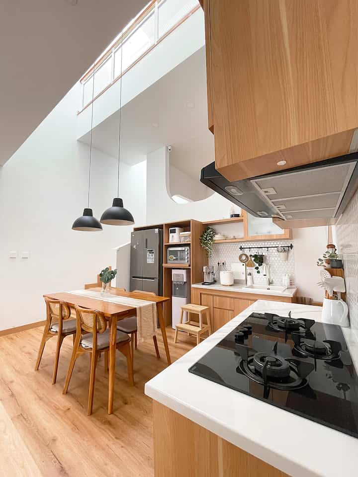 Modern kitchen with white walls and wood tone furniture, featuring dining table and pendant lights as key elements