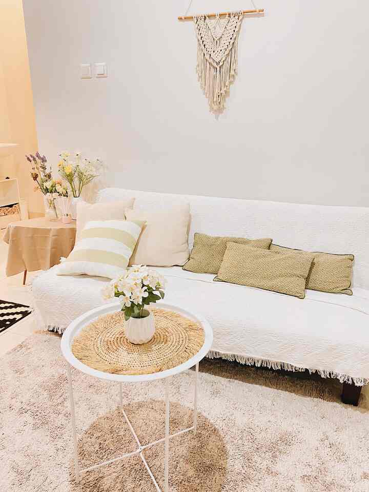White and beige-toned living room featuring a sofa bed, rattan table centerpiece, and natural decor creating a simple, cozy atmosphere