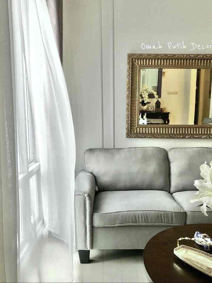 Gray and white toned living room featuring a central sofa, round coffee table, and a gold-framed mirror on upper right wall, creating a simple warm space
