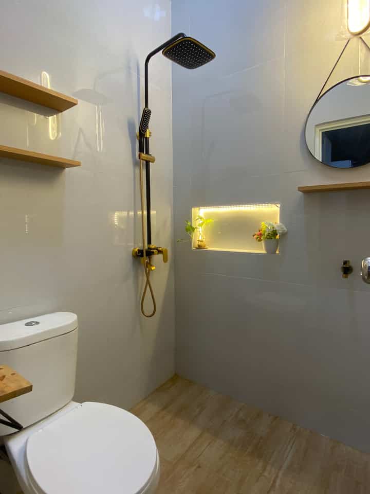 Minimal square bathroom in white and wood tones featuring gold shower fixtures and round mirror with cozy atmosphere