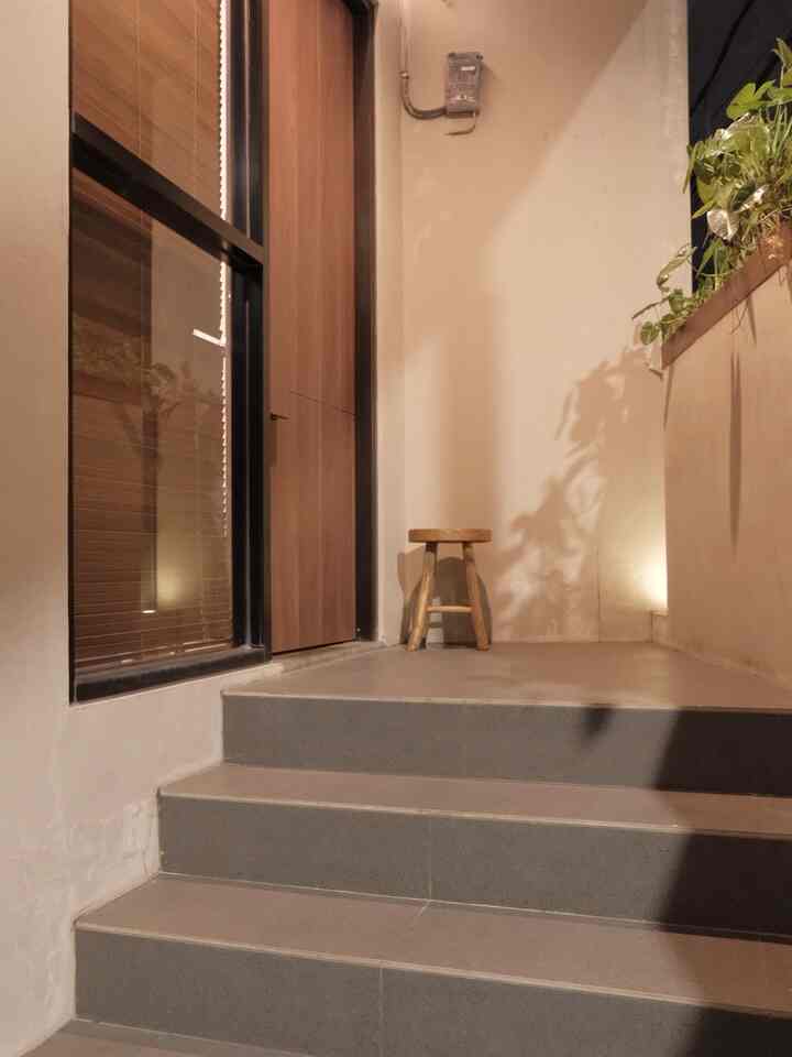 Natural tone entrance featuring wood door, gray tiled stairs, and a wooden stool creating cozy atmosphere
