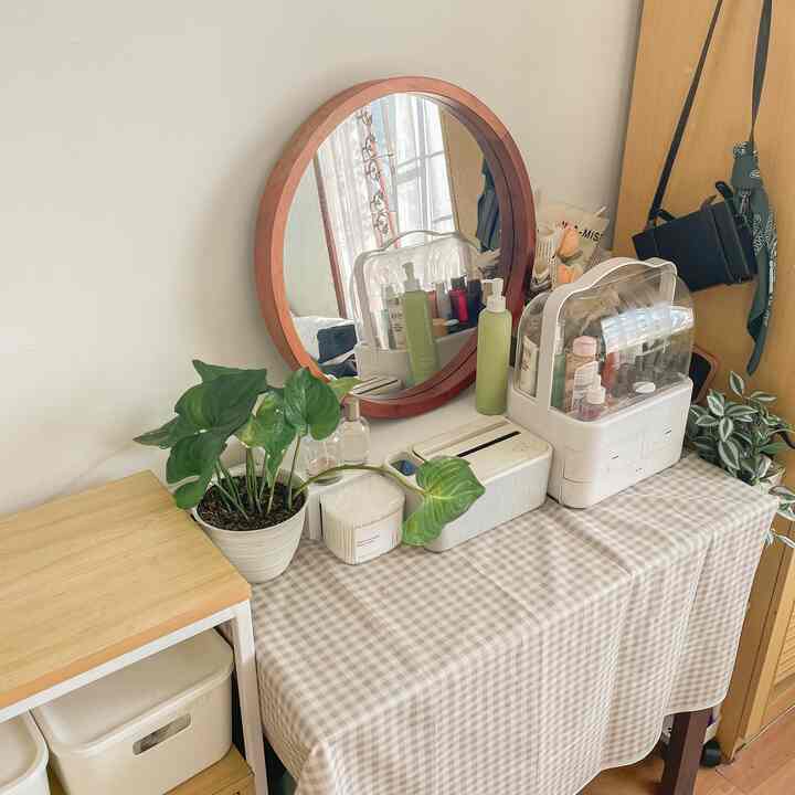 Minimal styled vanity area with white and wood tones, featuring a table, round mirror, and plant creating a cozy bedroom atmosphere