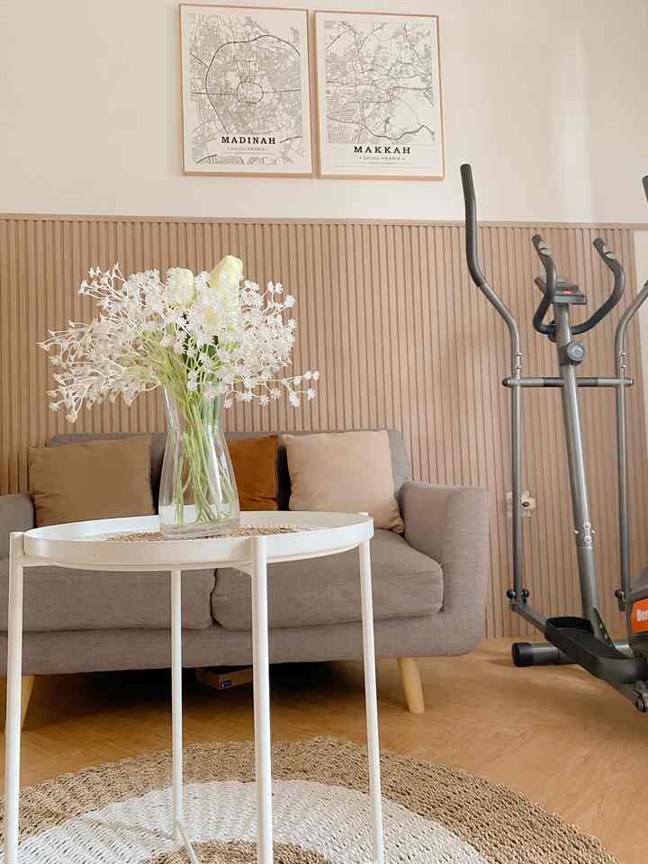 Natural-tone modern compact living room featuring a gray sofa, white side table with a flower vase, and exercise equipment