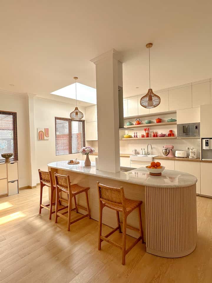 White and wood-tone Scandinavian kitchen space featuring a kitchen island, pendant lights, and dining chairs with a warm atmosphere