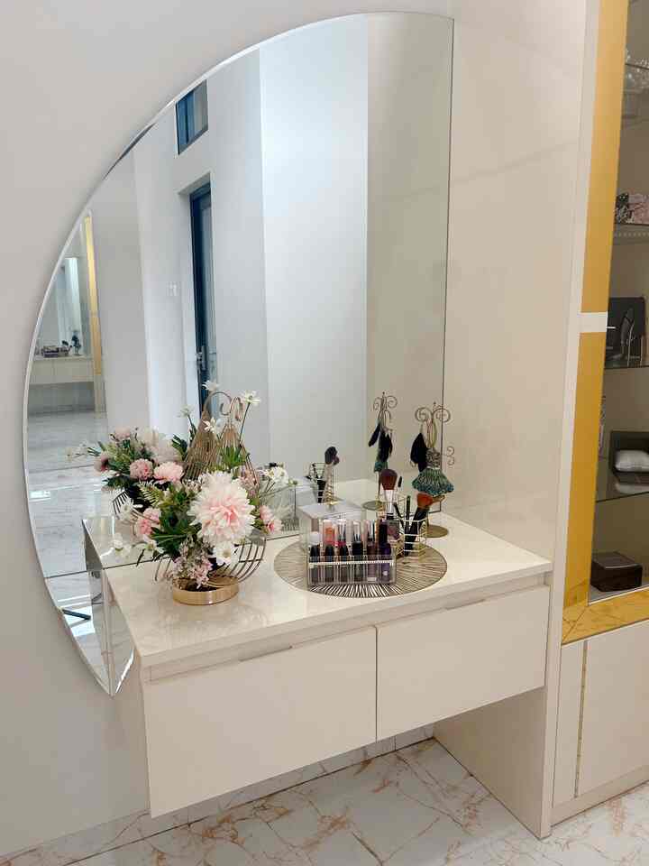 Beige and gold toned walk-in closet featuring a vanity table with floral arrangement and makeup, creating a clean space