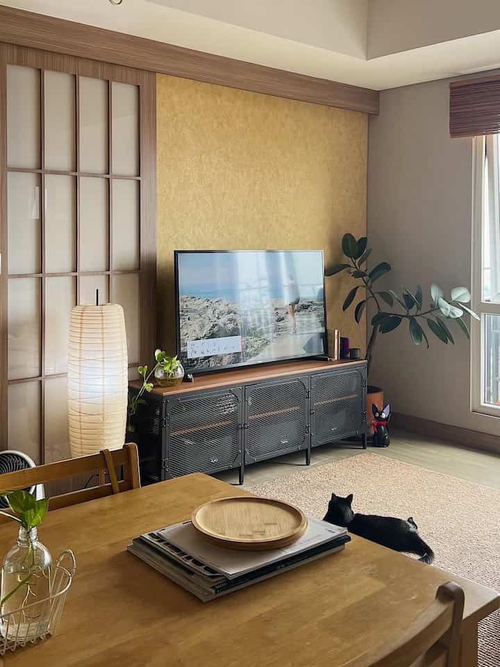Wood tone and beige living room featuring a black TV stand and a cat with a calm atmosphere