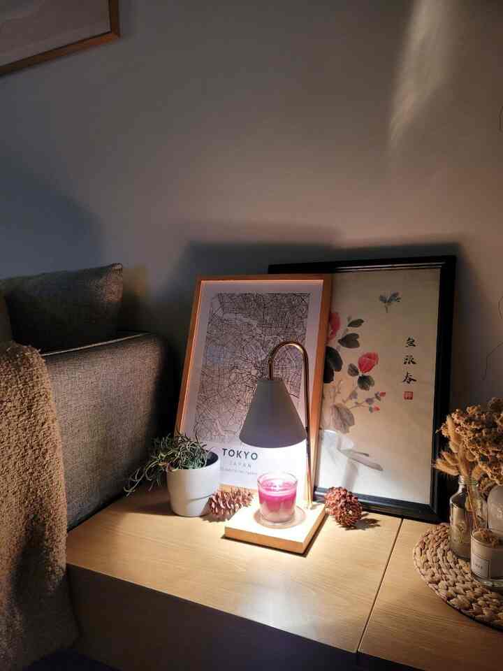 Cozy living room with warm wood tones and white hues, featuring a sofa, table lamp, candle, and Japanese-style framed art in a night setting