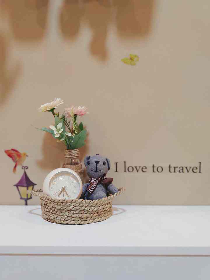 Natural kids' room decor with beige wall and white table featuring clock, plush toy, and flower vase