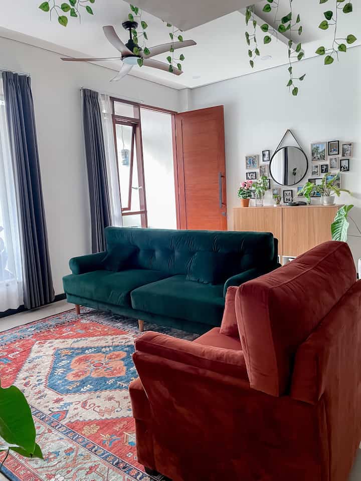 Bright bohemian living room with orange and emerald green sofas, plants, and natural wood elements