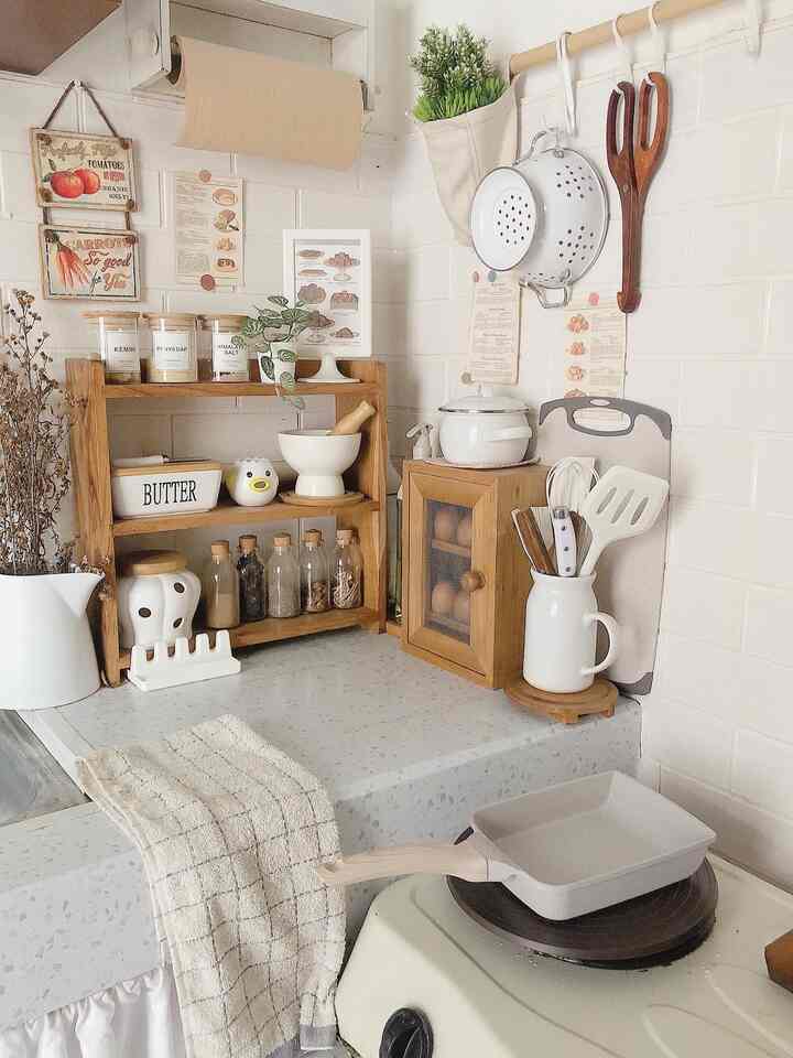 A compact kitchen featuring white and wood tones, neatly arranged storage rack and kitchen utensils creating a cozy atmosphere