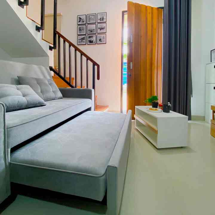 Soft gray-toned sofa bed placed in a clean living room with warm wooden door and staircase railing emphasizing natural ambiance