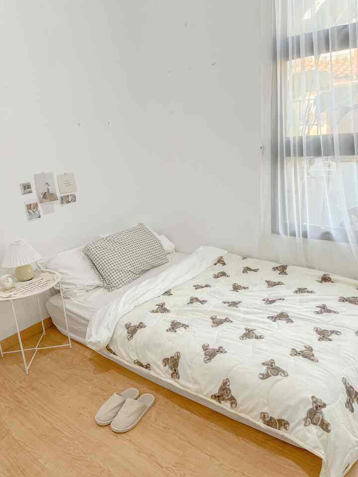 White and beige toned bedroom featuring a teddy bear patterned blanket and simple furniture arrangement, creating a clean and cozy space