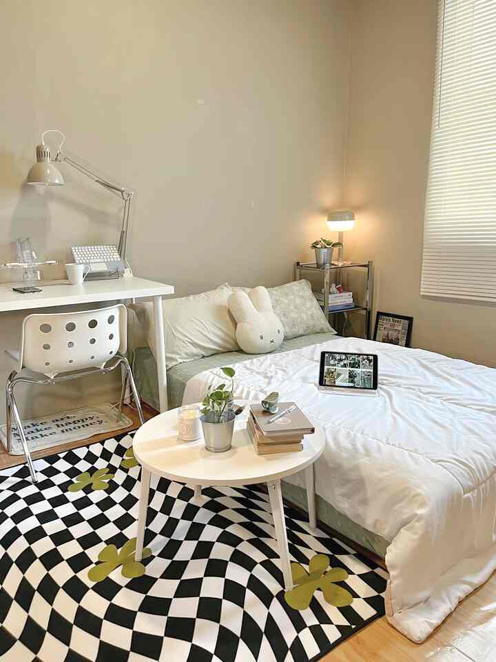 White and beige toned compact studio bedroom with simple furniture and checkered patterned carpet creating a cozy atmosphere