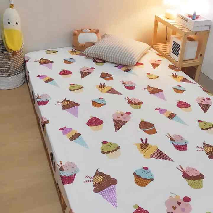 Kids' room with white walls and wood tone furniture, featuring playful ice cream patterned bedding and warm lighting for cozy atmosphere