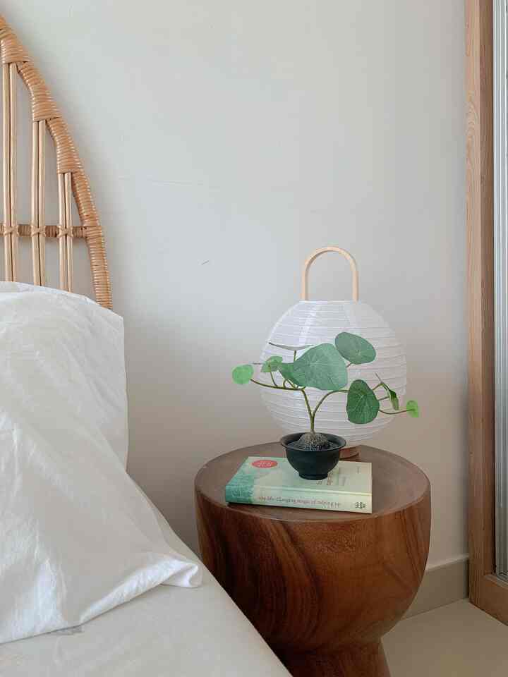 Natural wood tone nightstand with plant on white-toned bedroom, featuring a simple and calm Japandi-style interior