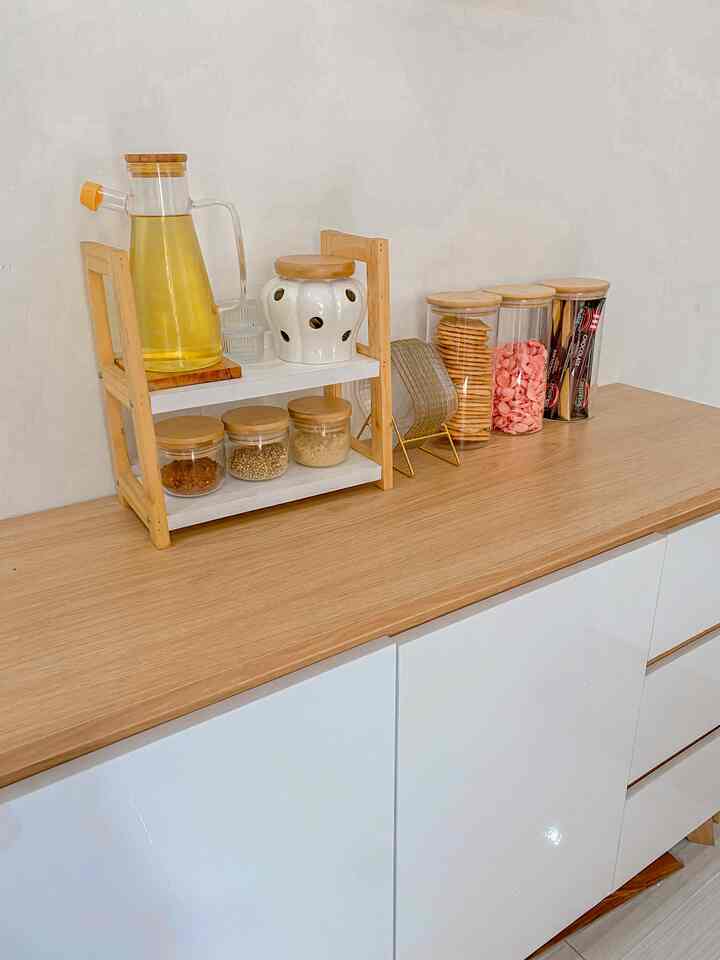 Natural-toned kitchen cabinet topped with transparent glass jars and wooden rack arranged neatly for storage