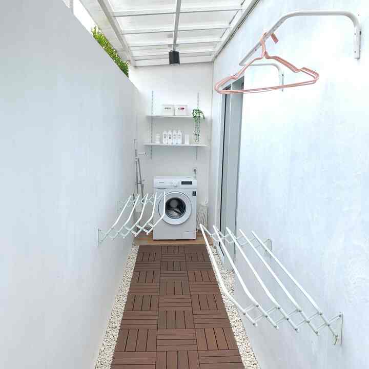 Bright natural-toned long and narrow laundry room featuring a white washing machine, wall shelves, and wood-tone deck tiles with a minimalist feel