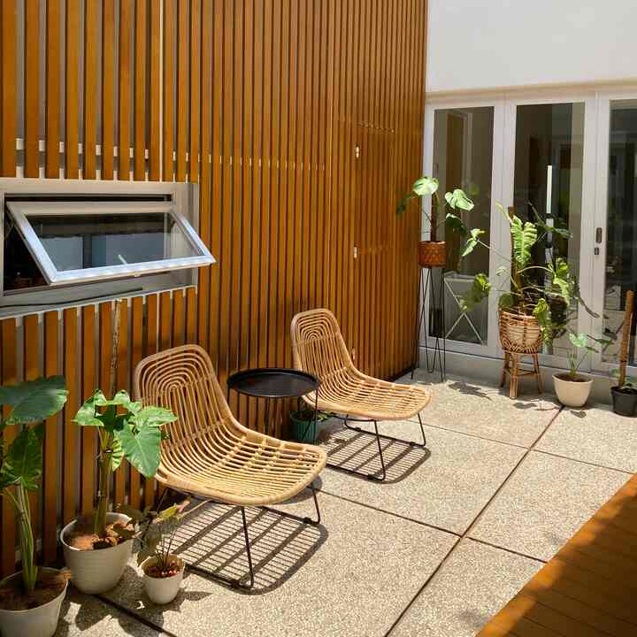 Warm yellow-toned wall with natural rattan chairs and plants arranged in a balcony relaxation space