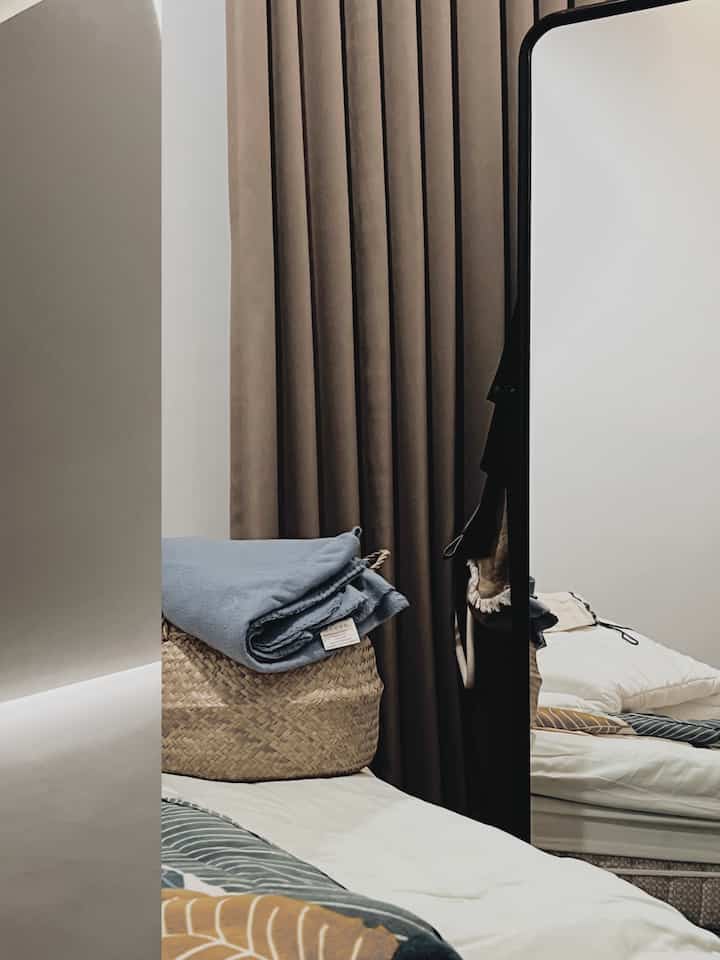 Natural tone bedroom space featuring beige curtains, blue bedding, and a woven sea grass basket creating cozy vibe