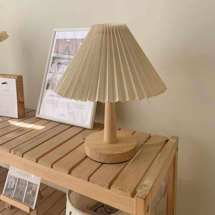 Beige-toned wall with a wooden wood-tone side table featuring a retro-style pleated lampshade lamp in a bedroom interior