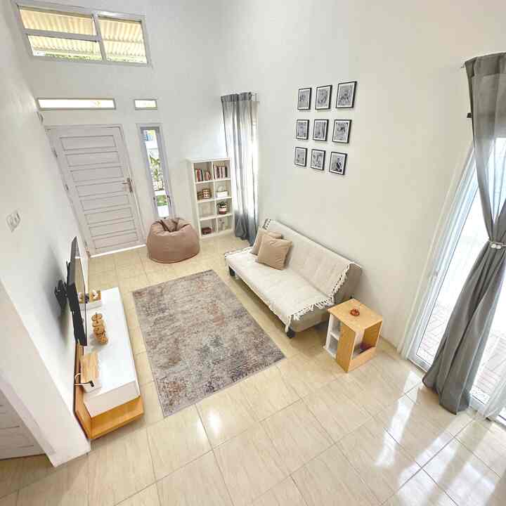 Bright white and beige toned small living room featuring a simple sofa, carpet, and picture frames in a cozy Japandi style