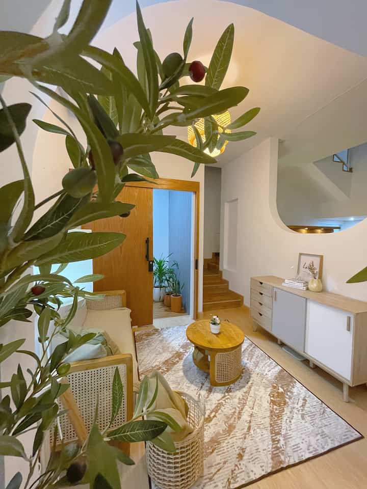 Natural wood tone and beige living room featuring rattan sofa, coffee table, and abundant plants with cozy atmosphere