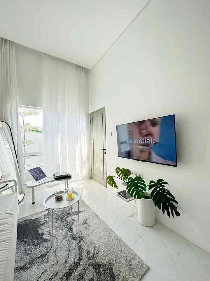 Bright and clean white-toned living room featuring a white sofa, side tables, and abundant natural light from large windows