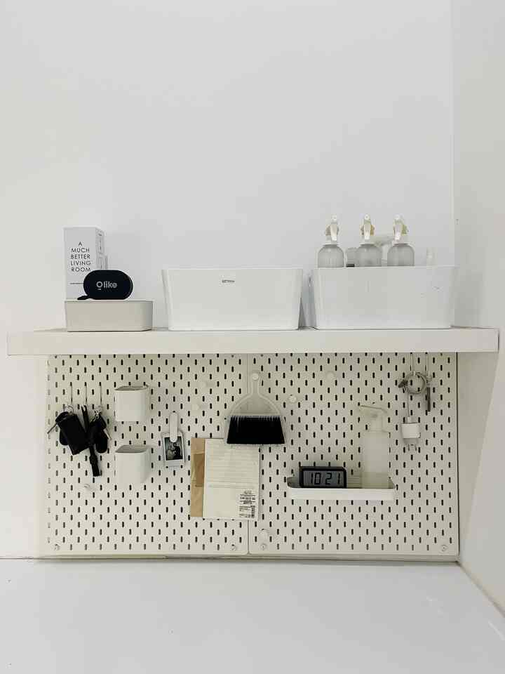 White-toned narrow utility storage space featuring IKEA SKADIS pegboard and organizers in a minimal laundry area.