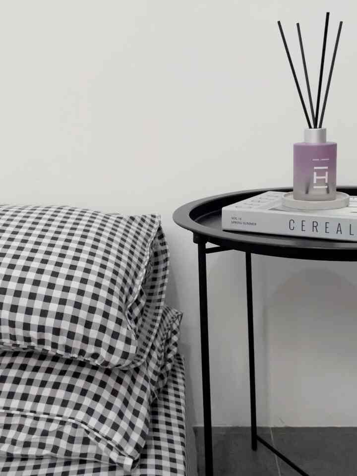 Simple and modern bedroom space with white walls, black and white checkered bedding, black metal nightstand, and a purple diffuser on a tray