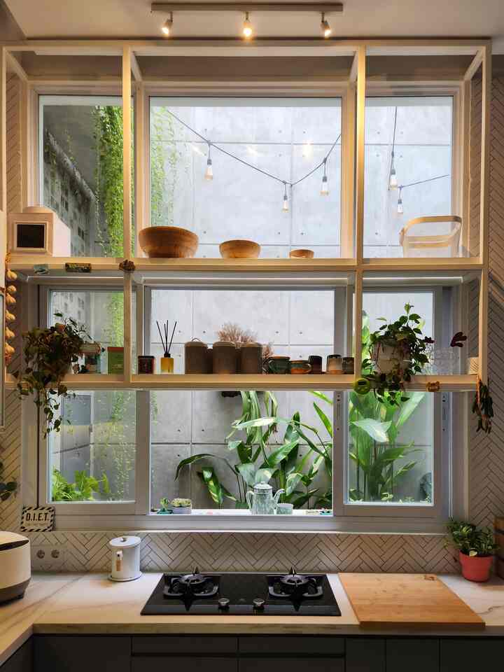 Bright kitchen space in white and black tones featuring large windows, plants, and a clean countertop with stove